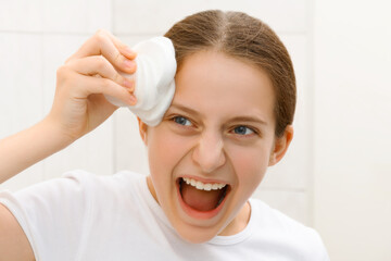 face of a screaming teenage girl, she looks at herself in the mirror and takes care of her skin,...