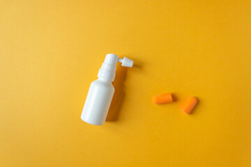 Top view of white ear spray bottle with nozzle and orange earplugs isolated on yellow background. Daily ears care.