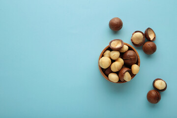 Peeled macadamia nuts in wooden bowl on blue background.