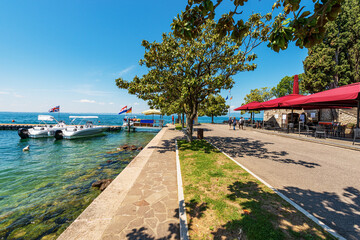 Promenade on lakeshore of Lake Garda (Lago di Garda) with a small wooden pier and two motorboats....