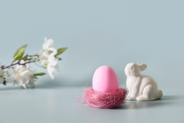 Easter pink egg in nest and bunny in spring composition on blue background. Happy Easter greeting card.
