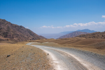 Fototapeta na wymiar Gravel road in the mountains with sky background. Road to Bartogay reservoir from Assy plateau.