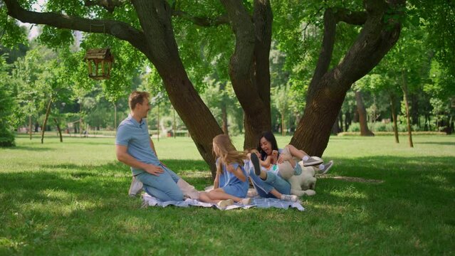Cheerful parents tickling kids on picnic. Family amusement on summer weekend.