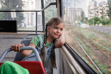 Young girl riding in empty tram and looking at the window dreamily, city tramway. Train lines are...