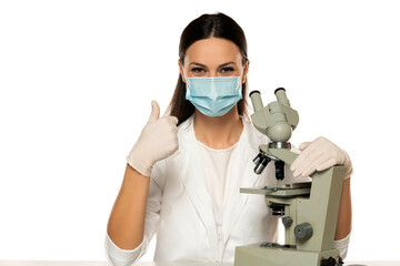 Fototapeta na wymiar Portrait of smiling female scientist with microscope and face mask, showing thumbs up