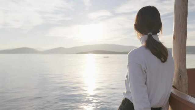 Shot of a woman standing by the sea and looking at it during golden hour.