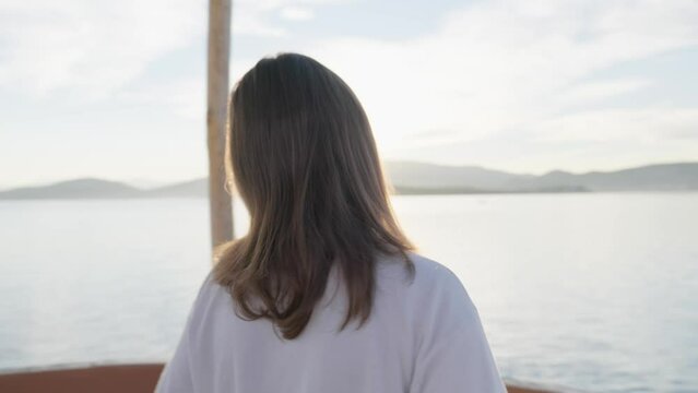 Medium closeup shot of a girl standing by the sea, gazing upon the sun while it sets.
