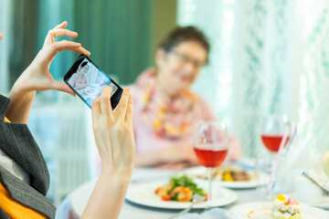 An elderly woman is photographed on the phone in a restaurant. focus on the phone. female hands holding a telephone