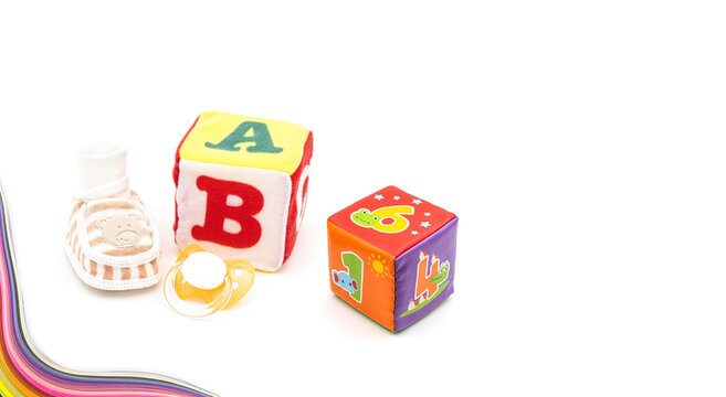 children concept with newborn boots, pacifier and plush cube on white background