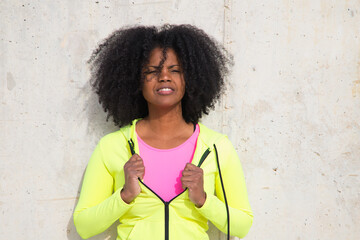 Obraz na płótnie Canvas Beautiful young Afro-American woman in bright green and pink sportswear on a grey concrete wall texture background. Woman makes different expressions. Laughing, serious, happy, sad, thinking
