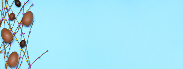 Tasty chocolate Easter eggs and spring branches on blue background with space for text