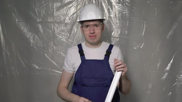 Builder in blue overalls and white hard hat helmet and glasses with angle square