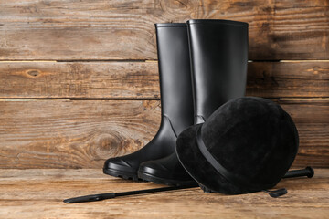 Horse riding helmet and boots with crop on wooden background