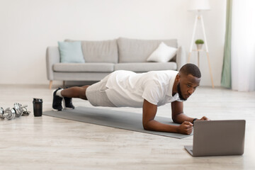 African Guy Exercising Standing In Plank At Laptop At Home