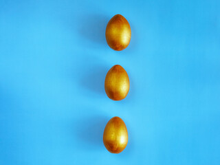 Three golden egg on the blue background. Design, visual art, minimalism. Flat lay top view, copy space. Happy Easter concept