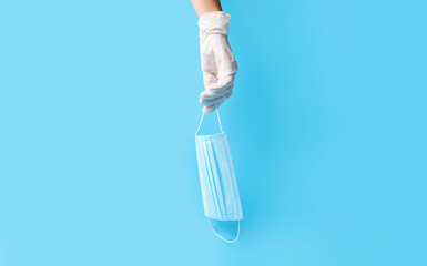 Female hand in rubber gloves with medical mask on color background