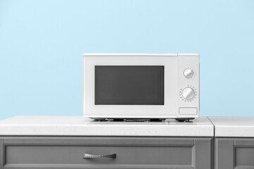 Modern microwave oven on counter near color wall