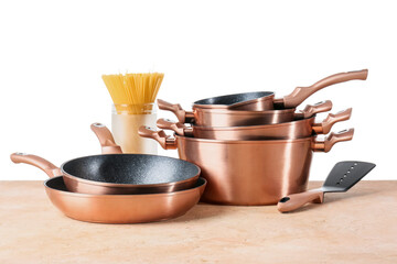 Set of copper kitchen utensils and jar with raw spaghetti on table against white background
