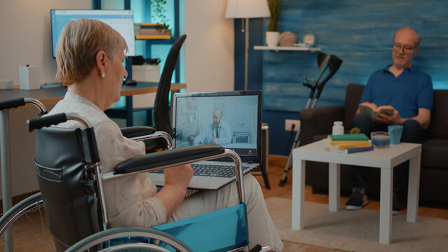 Elderly woman in wheelchair using video call to talk to doctor on laptop. Senior adult with physical disability meeting with specialist on online videoconference for telemedicine and telehealth.