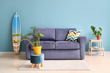 Interior of stylish living room with blue sofa, houseplants and surfboard