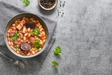 Spanish fabada served on gray background. Fabada makes of haricot, chorizo, morcillas or blood sausage, tomatoes. Top view. Copy space.