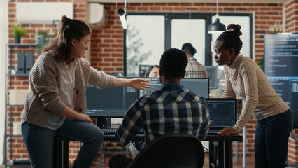 System engineer sitting on desk discussing with mixed team of coders about ai innovation in front...