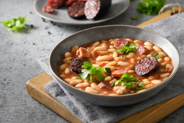 Spanish stew fabada with chorizo, morcilla, sausage, haricot served fresh toast on gray table. Close up. Traditional warming dinner.