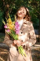 Young woman with bouquet of Gladiolus flowers enjoying sunny day in park