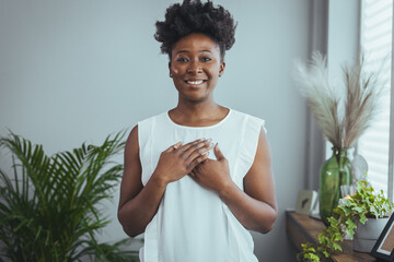 Portrait of happy millennial female volunteer holding folded hands on chest, looking at camera. Kind smiling young woman feeling thankful, showing appreciation, gratitude believe charity concept.