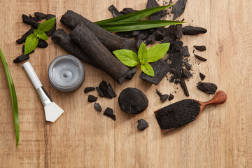 Flatlay of bamboo activated charcoal and charcoal mask and scrub decorate in wooden dish with green leaf in wooden background 