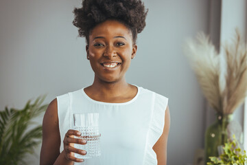 Close up beautiful african woman holding glass drinking a pill with still water. Minerals and...