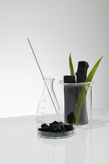 Activated charcoal research in laboratory with glassware beaker and transparent podium with green leaf and blank space in white background , front view