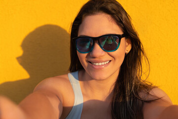 Hispanic Woman with sunglasses smiling with yellow background