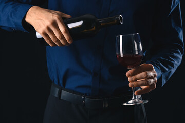 Young male sommelier with wine on dark background, closeup