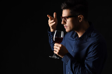 Young male sommelier tasting wine on dark background - Powered by Adobe