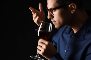 Young male sommelier tasting wine on dark background - obrazy, fototapety, plakaty