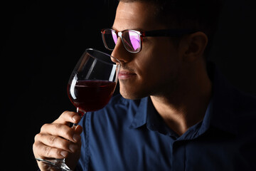 Young male sommelier tasting wine on dark background