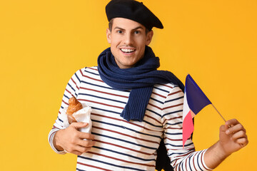 Handsome young man with flag of France and croissants on yellow background