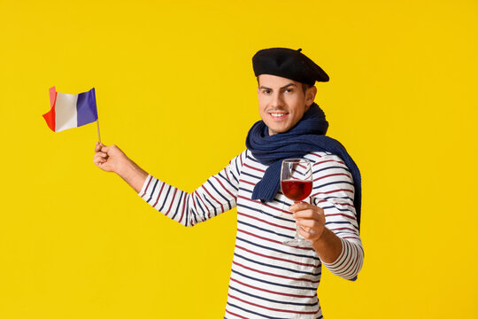 Handsome young man with flag of France and wine on yellow background