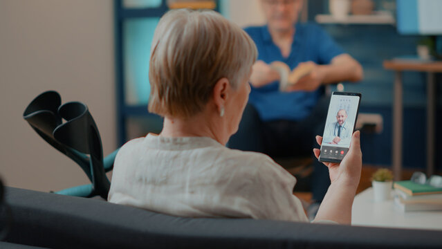 Senior adult talking to doctor on online videoconference, using smartphone for remote medical consultation. Woman with crutches chatting with specialist on telemedicine and telehealth call.
