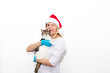 Cheerful young female doctor in Santa hat and gloves looking at camera with a cat isolated on white