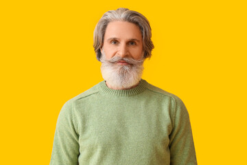 Obraz premium Handsome senior man in knitted sweater on yellow background