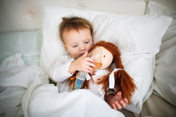 Cute baby with a doll with a nebulizer mask, a sick child in bed, bed rest during illness.