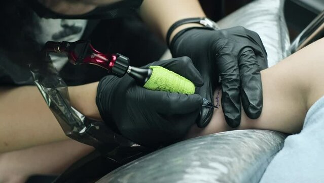 4K Slow motion footage. Closeup of a tattoo artist makes a tattoo on a woman arm. Professional tattooist works in studio. Tattooing machine.