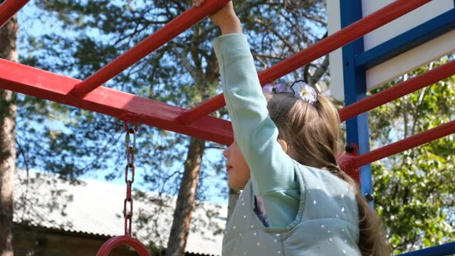 Active little girl climbing on monkey bars. Healthy activity for children. Child playing on outdoor playground.