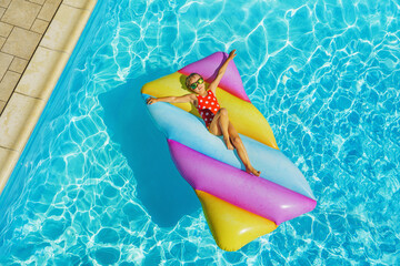 Child girl on the inflatable mattress in the swimming pool. Having fun on vacation at the hotel pool. Colorful vacation concept.