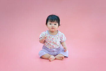 Asian baby smiling and sitting on pink color background. Cute 6 months baby sitting with copy space use as concept of valentine, love, learn, education, baby or kid department in hospital.