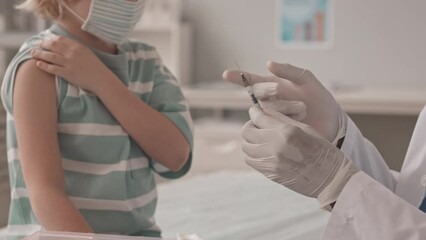 Cropped slowmo shot of African-American doctor giving vaccine injection to little boy sitting on medical couch in clinic - Powered by Adobe