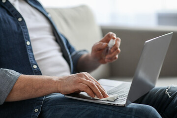 Male hands using disinfectant spray for cleaning laptop, closeup