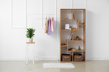 Rack with children's sweaters and shelf unit near light wall in room interior